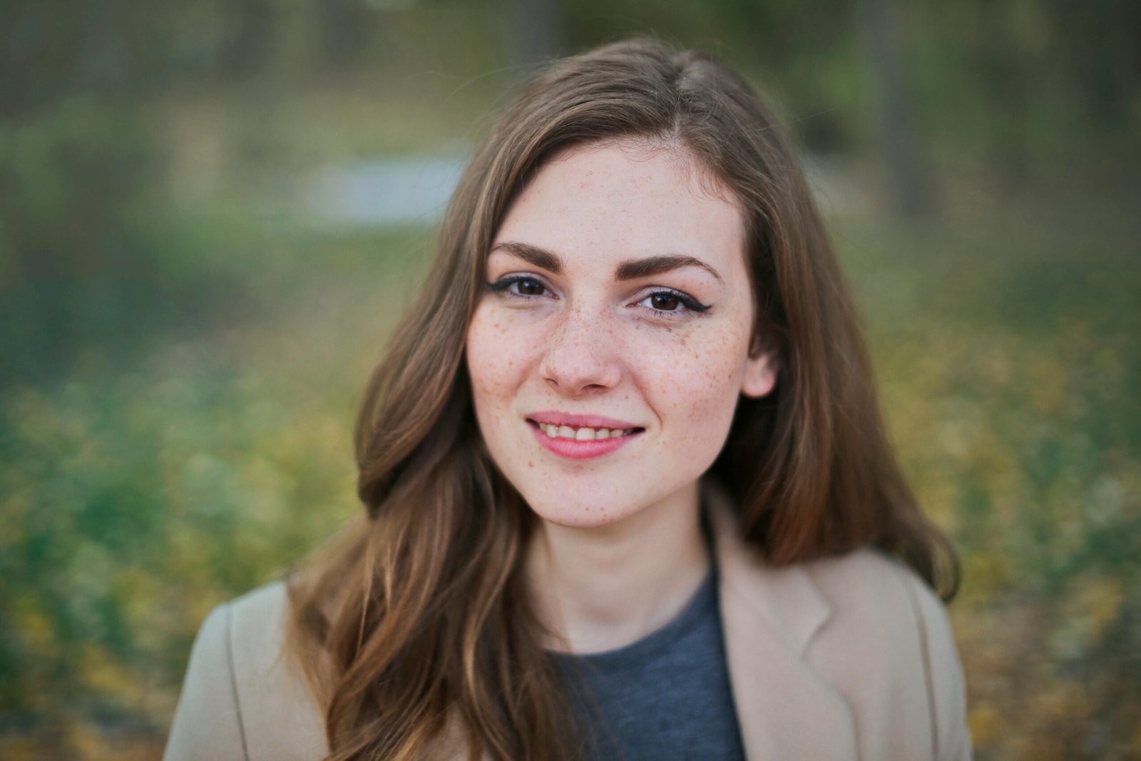 Close-up portrait of a smiling woman with freckles and long hair in a Budapest park during fall.